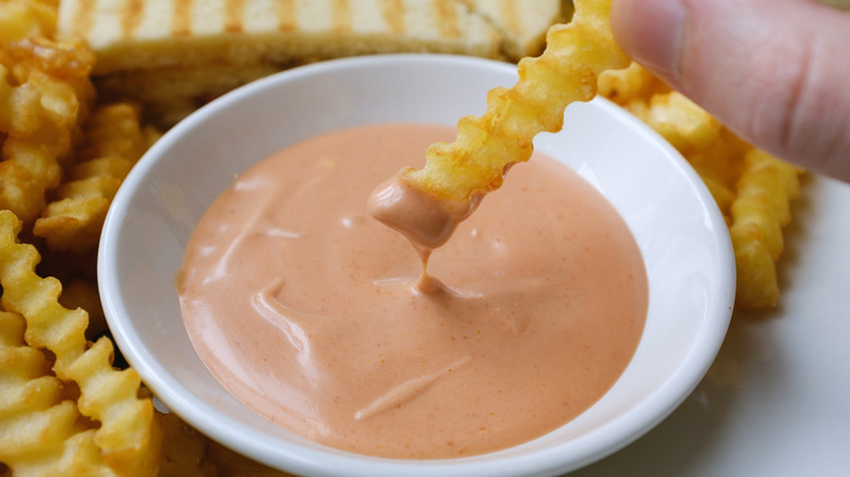 dipping a fry in orange colored sauce