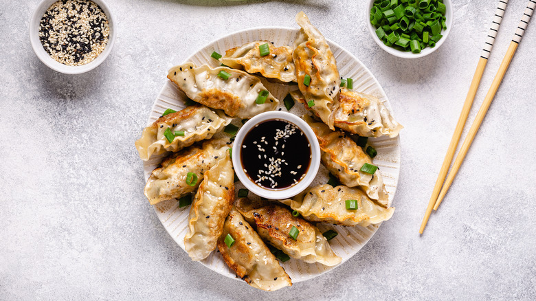 Crispy homemade gyoza on a white plate with scallions and sesame seeds sitting next to chopsticks