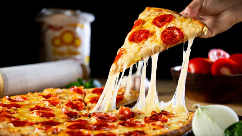 A hand lifting a slice of thin crust pepperoni pizza from the rest of the pizza