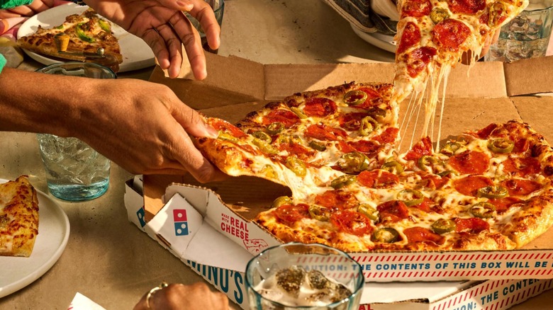 Hands reaching for slices of Domino's pizza from bix