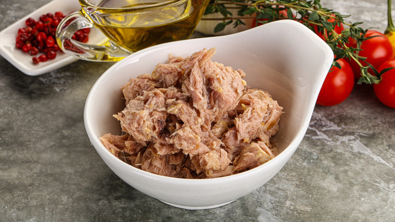 Canned tuna in white bowl with other ingredients in the background
