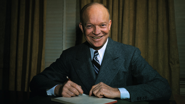 Dwight D. Eisenhower seated at a desk with a pen in hand