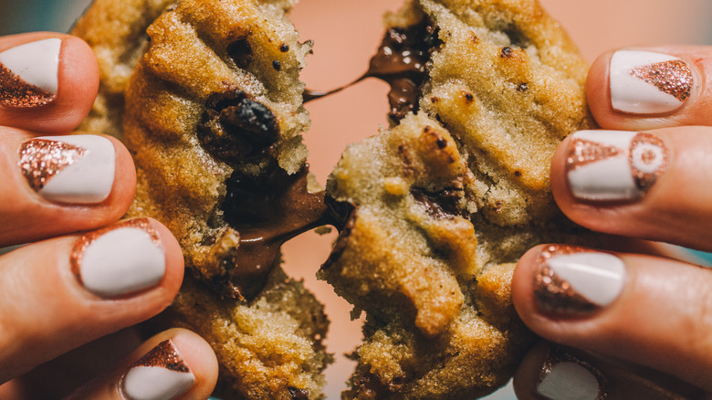 Hands splitting chocolate chip cookie