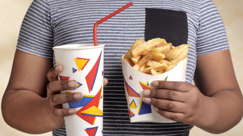 Person in a striped shirt holding a paper cup with a red straw and an order of fries