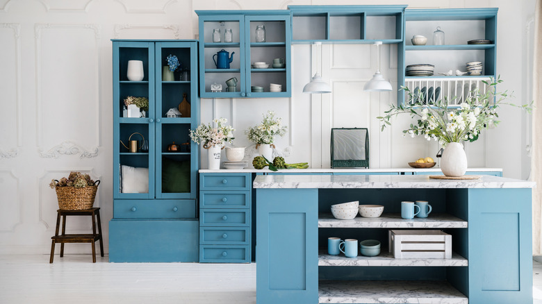 A modern kitchen with blue cabinetry featuring glass doors and open shelving