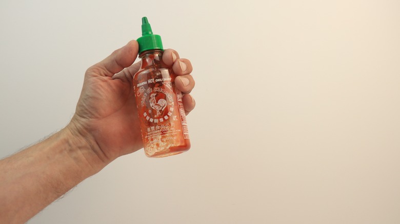 Hand holding empty sriracha bottle