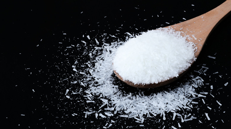Wooden spoon of MSG crystals spilling onto a black background