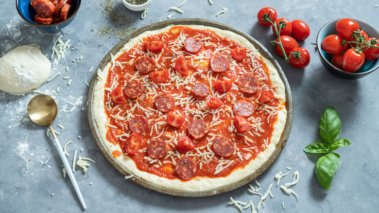 Raw pizza on pizza pan ready to be baked, surrounded by ingredients