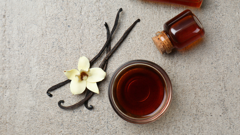 bowl filled with vanilla extract next to vanilla bean and flower