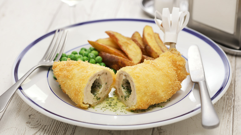 Chicken Kyiv, on a plate with potato wedges and peas