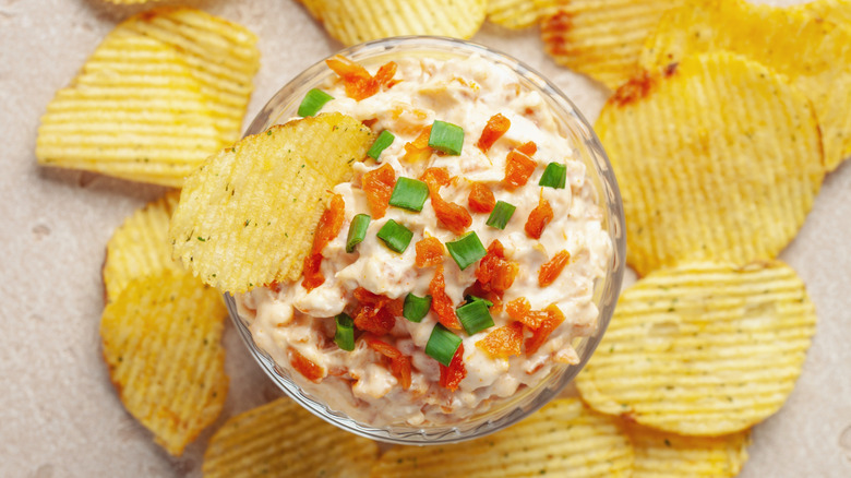 Bowl of French onion dip, decorated with finely chopped spring and caramelized onions, with chips