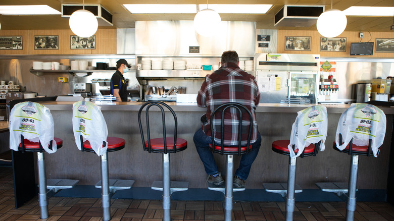 A man sits alone at a Waffle House counter while an employee works in the background