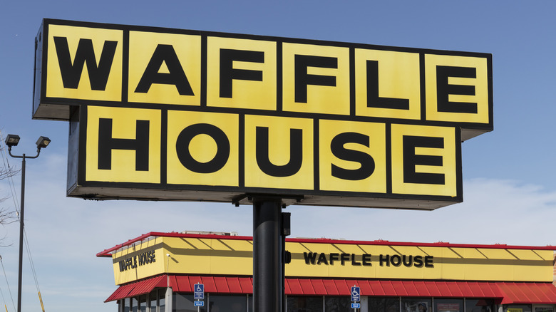 A Waffle House sign, with its characteristic yellow squares, with a Waffle House restaurant in the background