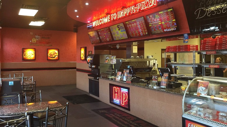 The bold interior of a Happy's Pizza restaurant featuring red neon lights and a diner style feel