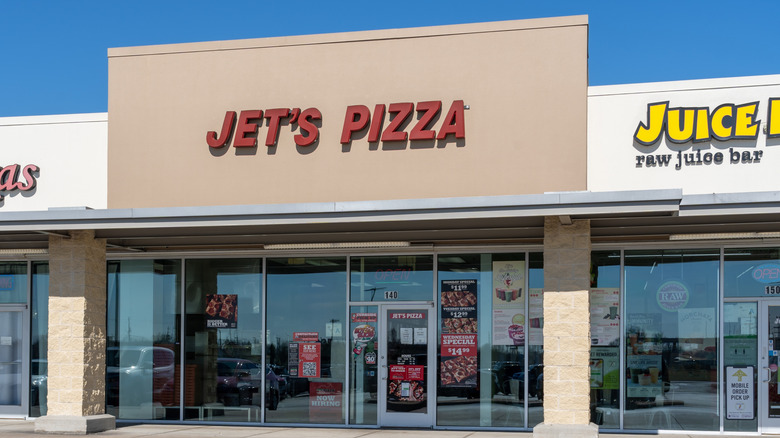 A Jet's Pizza storefront entrance with red branded signs advertising deep dish pizza specials