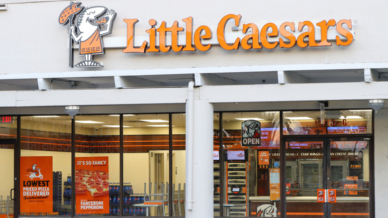 The exterior entrance of a Little Caesars pizza restaurant with orange signs advertising low prices and fancy pepperoni