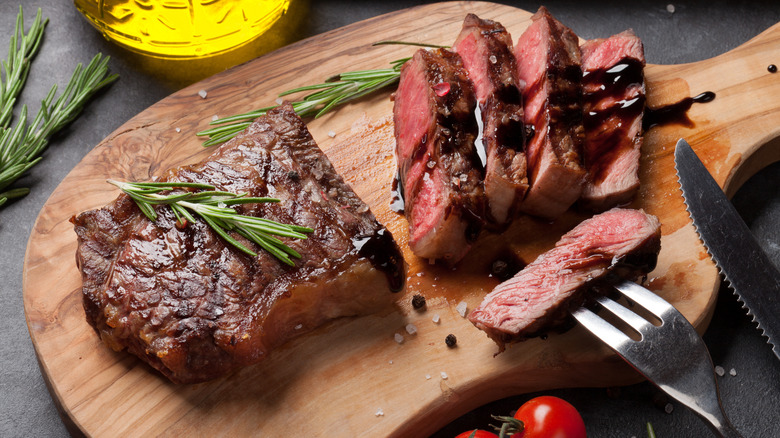 Sliced steak on a cutting board with rosemary