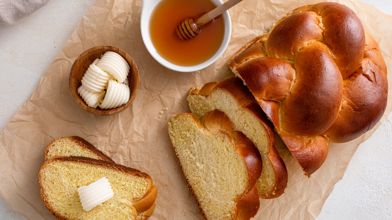 Sliced loaf of Challah bread with butter and honey on the side on a brown paper.