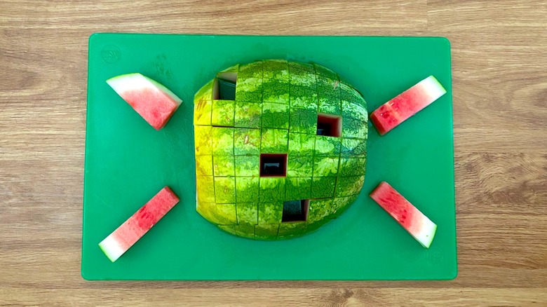 Watermelon cut into a grid pattern with sticks removed on green cutting board