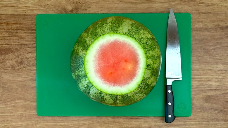 Watermelon with end cut off and chef's knife on a green cutting board