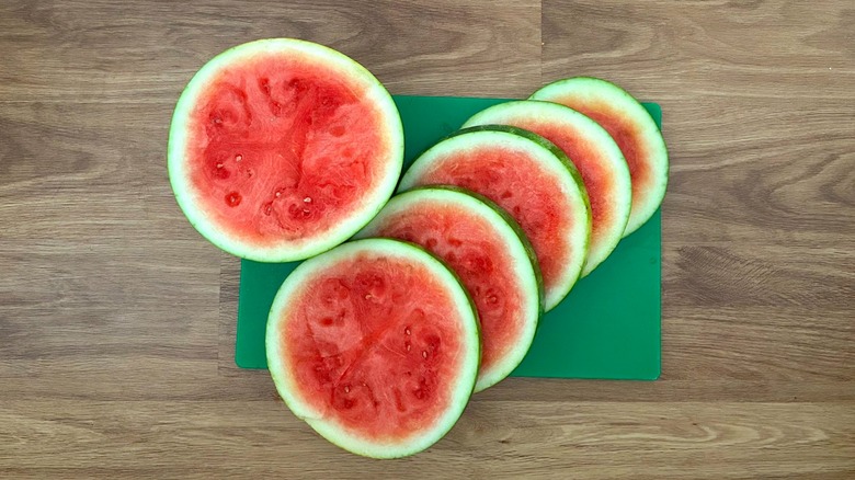 Watermelon cut into round slices on a green cutting board