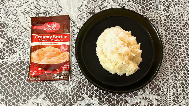 A plate of mashed potatoes next to a packet of Betty Crocker Creamy Butter Mashed Potatoes