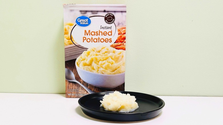 A plate of mashed potatoes in front of a box of Great Value Instant Mashed Potatoes