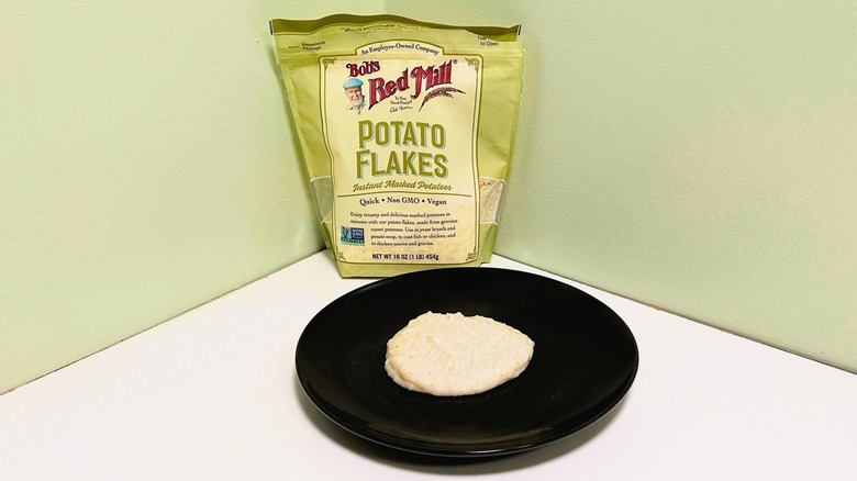 A plate of mashed potatoes in front of a bag of Bob's Red Mill Potato Flakes