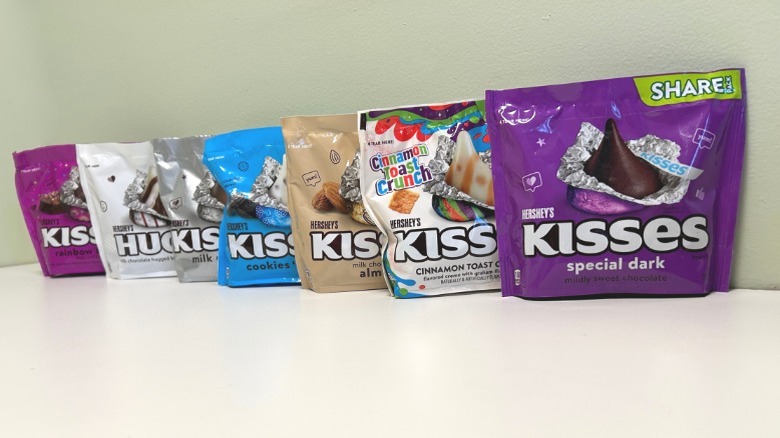 Seven bags of Hershey's Kisses flavors in a row against a green and white background