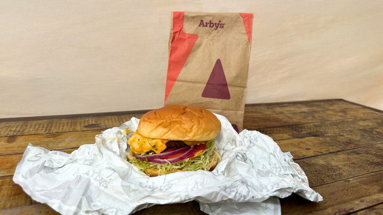 An Arby's cheeseburger in front of the fast food takeout bag
