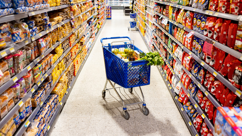 A shopping cart in the middle of a grocery aisle, surrounded by highly-processed foods