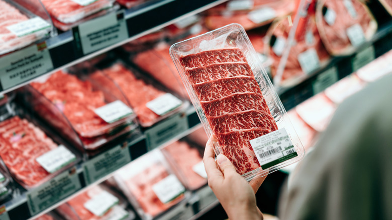 person holding packaged red meat in meat aisle of grocery store