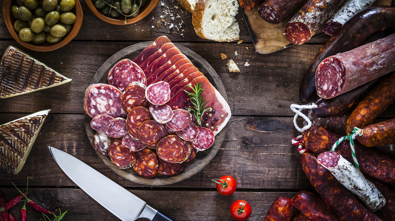 cured meats on wood cutting board surrounded by snacks
