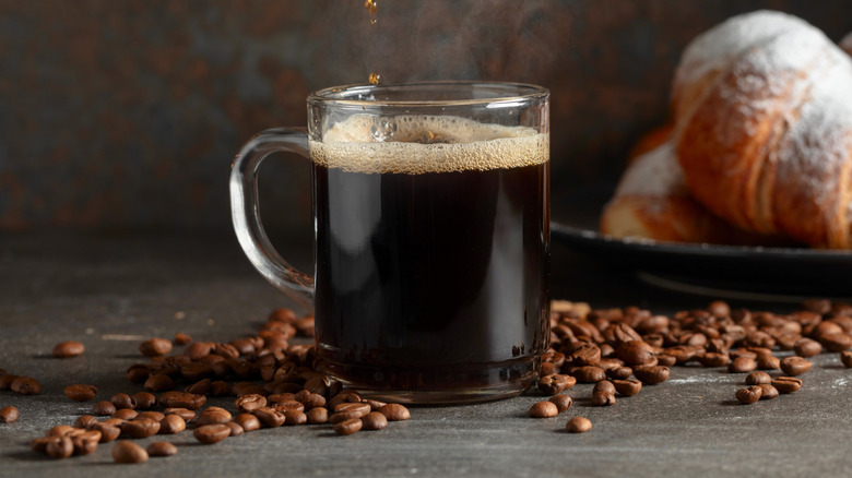 Coffee being poured into a mug in front of croissants
