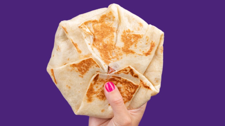 hand holding Crunchwrap over purple background