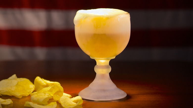 a schooner beer glass next to a basket of potato ships set against a dimly lit American flag