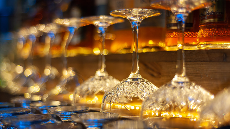 A line of crystal wine glasses, open side down, on a backlit bar