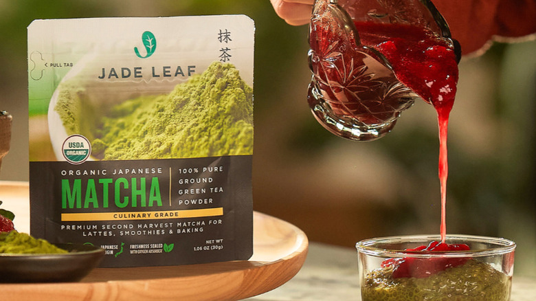 Package of Jade Leaf matcha next to a small crystal pitcher of a red substance being poured into a glass