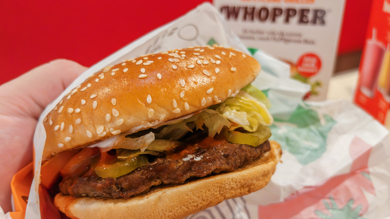 Person holding a Burger King Whopper in wrapper.