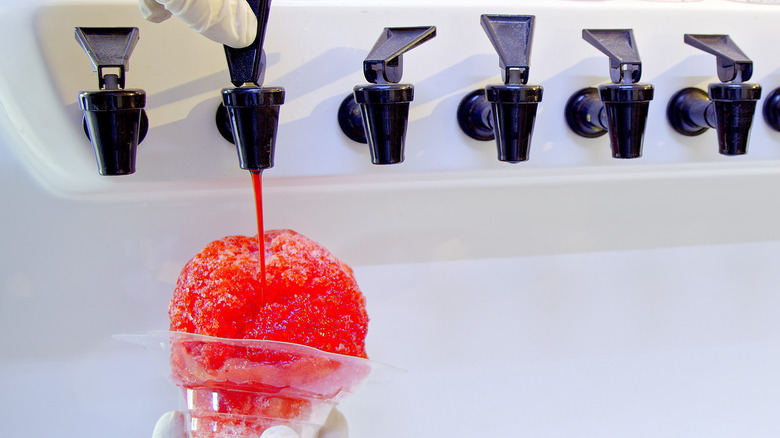 person pouring red syrup on snow cone