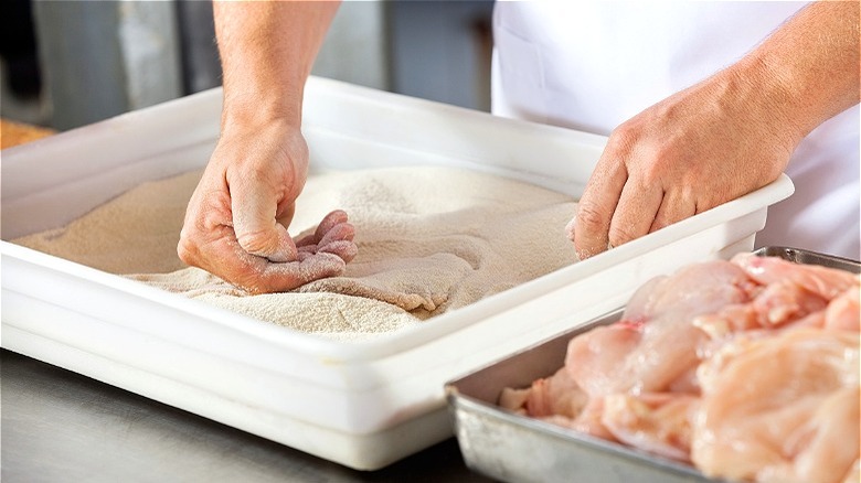 Hands dredging chicken in coating