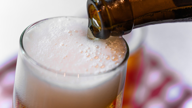 Close up of beer being poured into a glass with lots of foam.