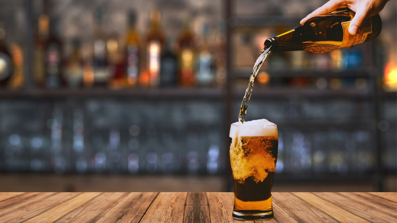 bottle of beer being poured into a mug on a wood bar counter