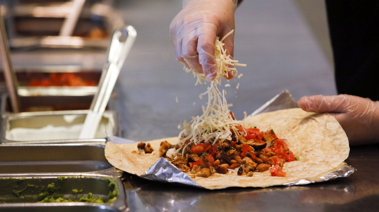Employee sprinkles cheese onto Chipotle burrito