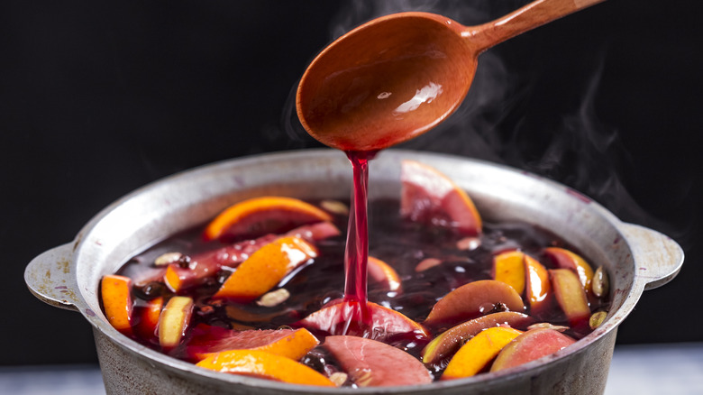 A steaming silver pot with sliced fruit and red wine