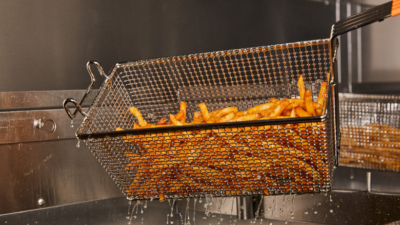 Freshly-fried french fries from Popeyes being lifted out of a fryer with a metal basket