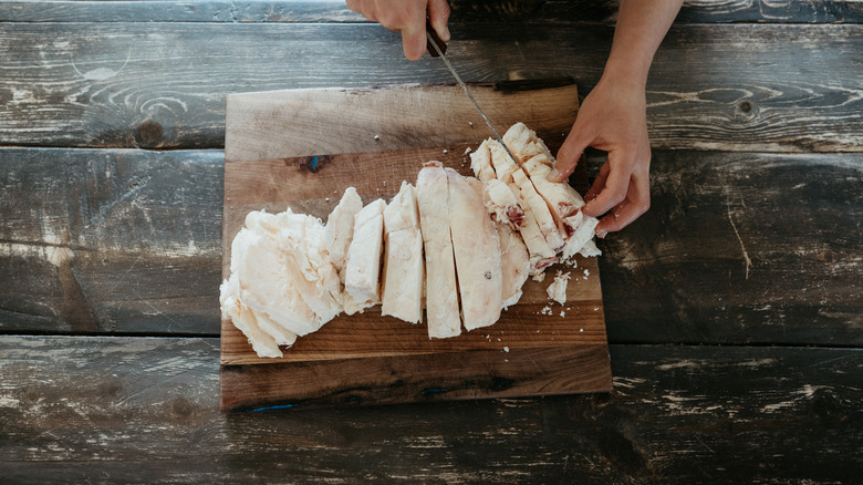 Hands slicing beef fat on wooden cutting board
