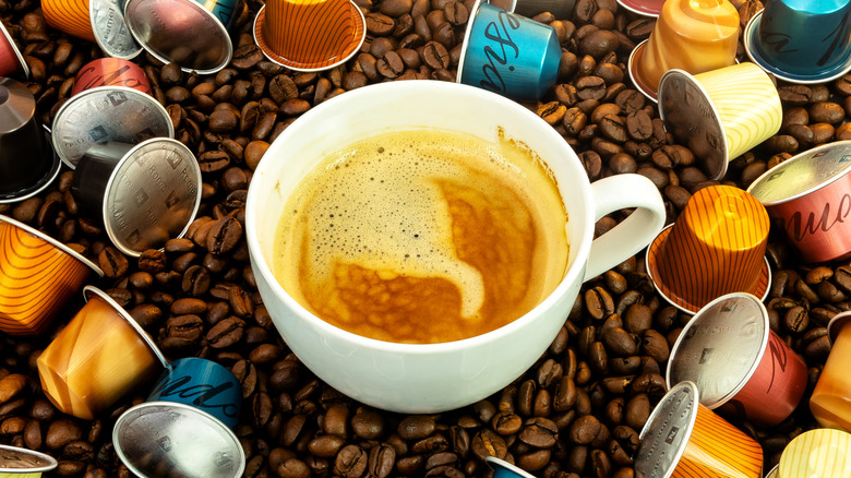 cup of espresso surrounded by whole beans and Nespresso pods