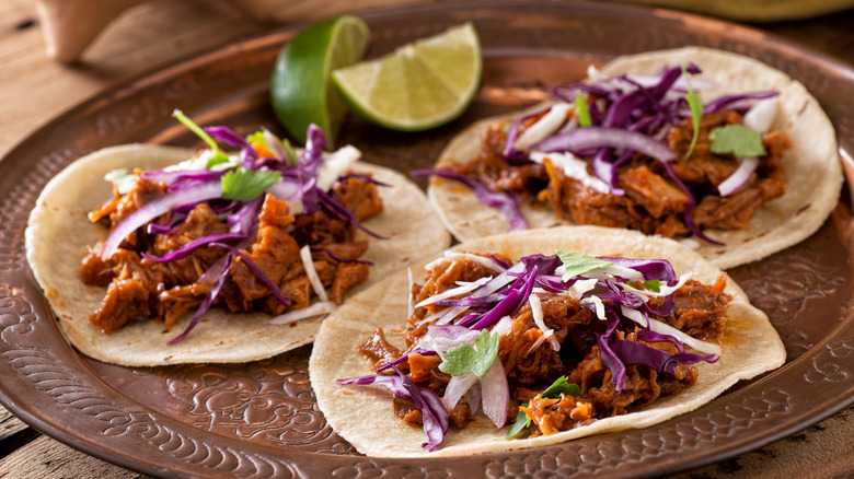 three opened pulled pork tacos and lime wedges