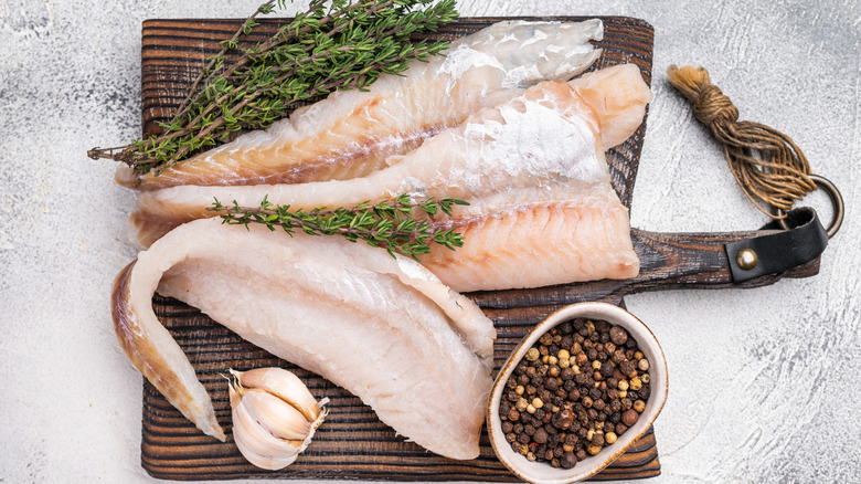 Raw pollock fillets on wooden board.